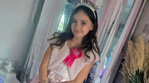 Family handout Aria Thorpe. She has long dark hair and is wearing a pink dress and a headband that reads "Happy Birthday". She is also wearing a hot pink birthday badge. She is looking directly at the camera and smiling.