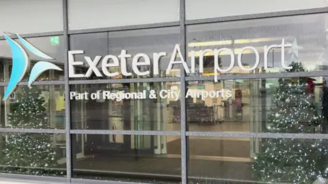 Glass fronted entrance to Exeter Airport Departure Hall, with the name of the airport on the windows.