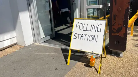 A polling station sign outside a building in Guernsey. A person is walking into the building.