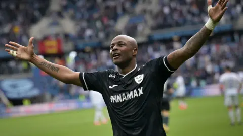 Ghana forward Andre Ayew, playing for French side Le Havre in a black top, spreads his arms out wide while celebrating a goal for his team 