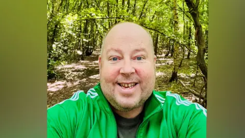 James Hillery James Hillery photographed in a woodland wearing a bright green sports top and smiling at the camera