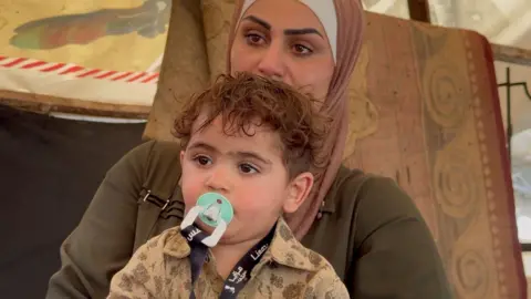 Veiled woman, eyes filled with tears, holds her son in her arms in Gaza