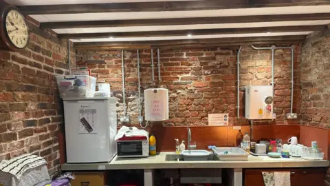 BBC/Tim Dale A collection of kitchen units including a sink, fridge and microwave, all built at waist level against a brick wall