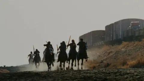 Sippy Films A shot from the film Sholay shows men in silhouettes wielding weapons and riding horses, leaving behind a white film of dust.