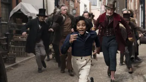 Dean Rogers/Lionsgate UK A scene from The Personal History of David Copperfield, directed by Armando Iannucci. Showing actor Jairaj Varsani in Victorian dress being chased by Peter Capaldi.