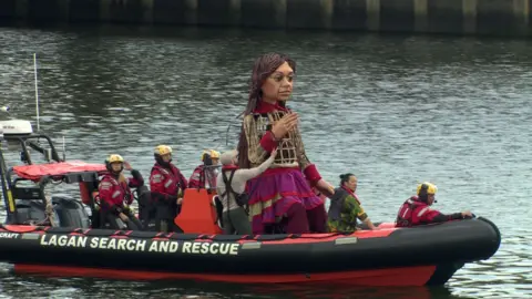 Large puppet with handlers, Little Amal on a Lagan Search and Rescue boat