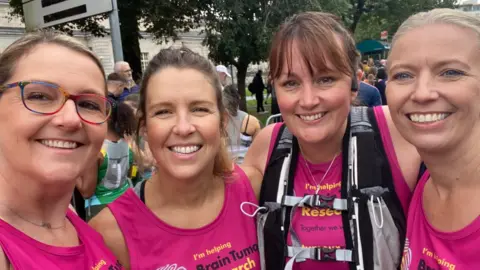 Brain Tumour Research Ms Wrathall smiles into the camera with a friend standing to her left and two women standing to her right. They're all wearing pint Brain Tumour Research running vests.