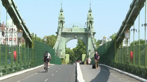 A Victorian bridge with ornate pillars looking south - there are cyclists and pedestrians using the bridge - its ironwork is painted green.