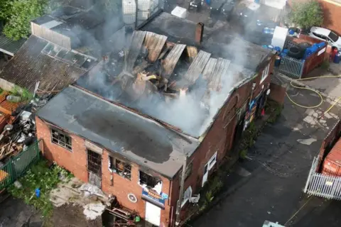 Supplied An aerial image of a two-story commercial building with a fire-damaged roof. Smoke is rising from the roof.