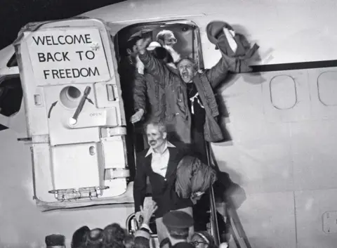 Getty Images American hostages leave the plane with their arms in the air, next to a sign that reads: Welcome Back to Freedom