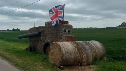 March YFC Straw bales shaped into a combine harvester, with rectangular bales making up the driver's cab and the grain tank, while the conveyor and cutter bar in front of it is made from round straw bales 