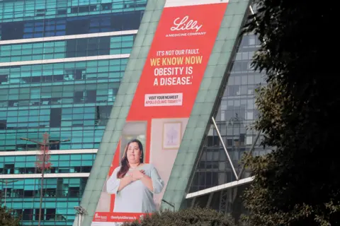 Reuters A hoarding of Eli Lilly on a building in Gurugram, India, shows a woman wearing a tunic with her hands on her heart. The tagline says - "It's not our fault. We know now obesity is a disease."