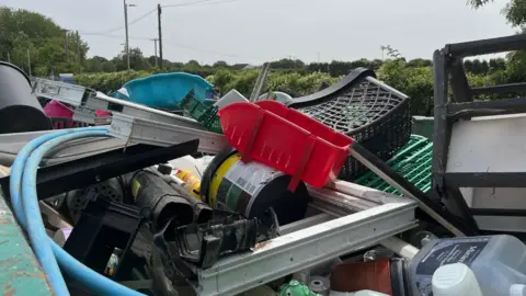 The top of a waste container at a household recycling centre - lots of different plastic items, including old shopping baskets, containers and a PVC window frame.