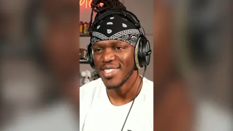 Man with a bandana and headphones on in a white t shirt.