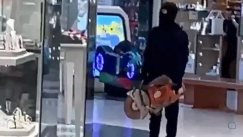 YapApp Man in balaclava stood outside shop with circular saw