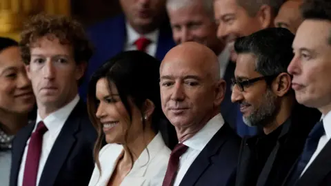 From left to right: Meta CEO Mark Zuckerberg wearing a navy suit, red neck tie and white dress shirt; Lauren Sanchez, wife of Amazon founder and former CEO Jeff Bezos, wearing a white blazer; Jeff Bezos, in a navy suit, red neck tie and white dress shirt; Google CEO Sundar Pichai, in an all black coat, shirt and tie.