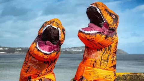 The heads of two of the T. rex costumes with Douglas Bay in the background.