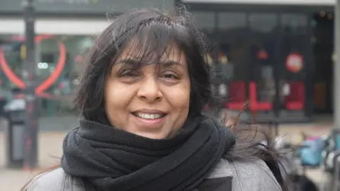 Jamie Niblock/BBC Rasna Patel in Harlow town centre, wearing a scarf and smiling