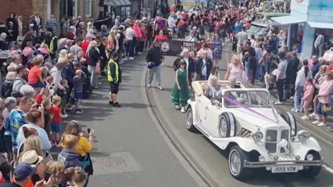 BBC A vintage white car driving through crowds in Fleetwood
