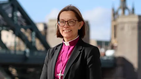 Diocese of Newcastle Bishop of Newcastle Helen-Ann Hartley wears a pink robe and brown glasses