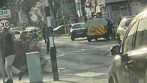 Supplied A photo taken from across the road shows three police vehicles, including a van, parked on the street. Armed police officers dressed in black vests and helmets can be seen