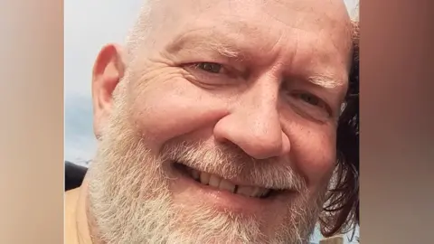 Balding middle-aged white man with cropped white hair and beard 