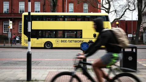A cyclist cycles past a yellow Manchester bus on Oxford Road.