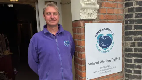 George King/BBC Nick Chaplin standing in the doorway of the Ipswich and District Animal Welfare Centre. He is wearing a purple jumper with the charity's logo on it.