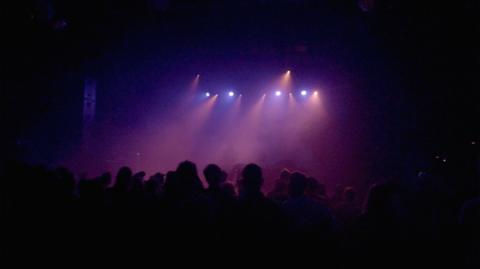 A crowd facing a stage with purple lighting