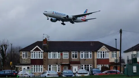 A plane flies over homes near Heathrow Airport on an overcast day