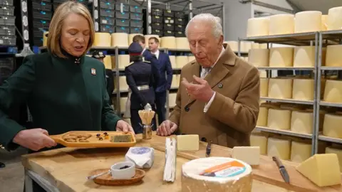 PA Media King Charles III is offered some cheese by third generation owner Gill Hall during his visit to the newly opened Butlers' cheese campus at Butlers Dairy, Preston.