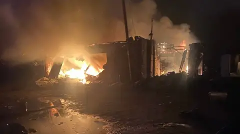 A fire with lots of smoke surrounded by multiple derelict buildings 