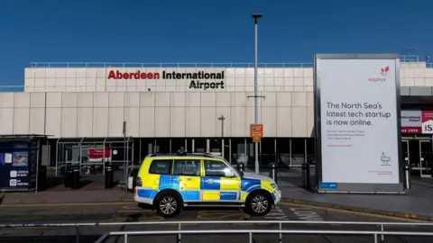 The front entrance of Aberdeen International Airport with a police car parked outside