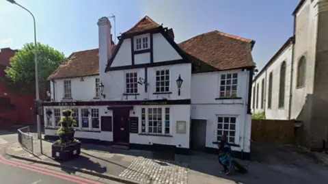 A Google Maps picture of the Rising Sun Inn, a largely white building with black beams on the outside of it.