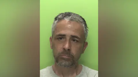 A mugshot of an unshaven man against a green background