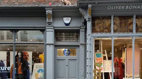 York Civic Trust An image of the shop door above which is the stained glass blue plaque