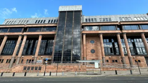 Imposing court building made from red stone walls and columns with large dark windows.