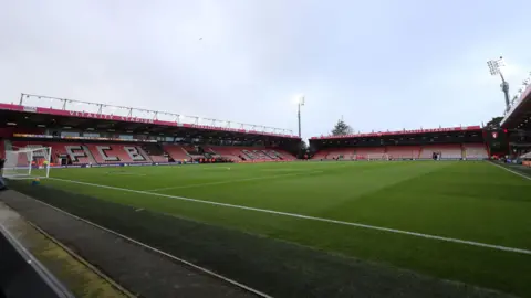 Reuters The football pitch at the Vitality stadium viewed from a corner to the right of one of the goals. The empty single tier stands have red plastic seats with some black and white seats spelling out AFCB. 