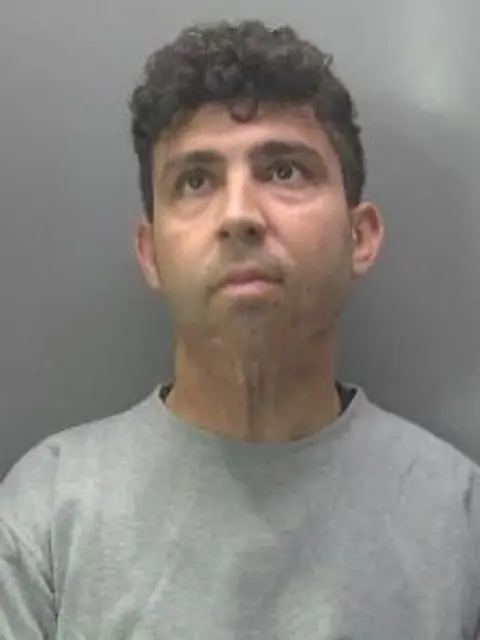 Cambridgeshire Police A police image of a man with dark curly hair wearing a grey, round-necked T-shirt.