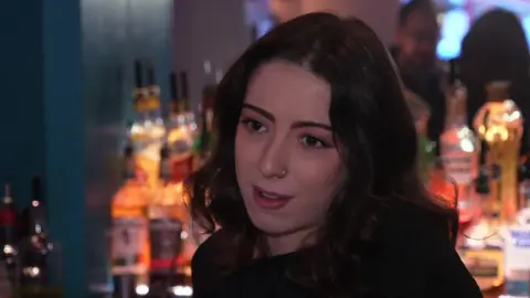 BBC / Peter Whittlesea A woman with dark hair is standing inside a pub.
