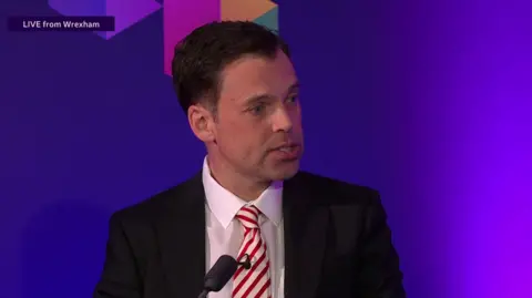 BBC Ken Skates speaking in the debate in Wrexham, wearing a dark suit and red and white striped tie