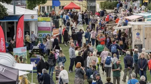 IOM GOVERNMENT Crowds of people walking around food stall at the food festival.
