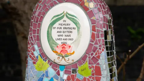 Eleanor Bentall A multicoloured mosaic memorial on a bench erected after residents of cardboard city were evicted. a painted tile in the middle reads, 'in memory of our brothers and sisters who have lived and died here', with leaf tiles underneath containing handwritten names