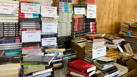 Piles of books on a table with labels attached. 