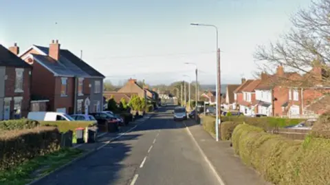 A main road is pictured with houses either side.