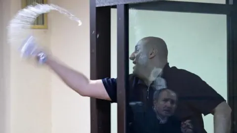 A man behind a glass window is pictured throwing water out of a glass