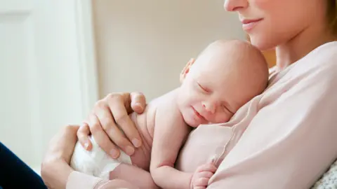 A woman holds a baby as it sleeps against her.