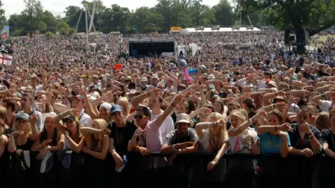 PA Media Crowds of people, many of them waving their arms, facing the stage at V Festival in Hylands Park on a sunny day. The photo is taken from the stage.