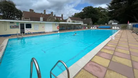 An outdoor pool with a swimmer swimming lengths to keep fit.