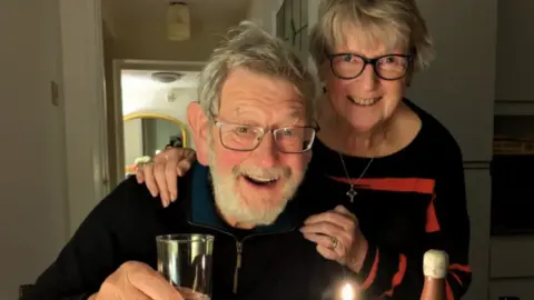 supplied An elderly man and woman pose together for a photo smiling and raising their glasses.
